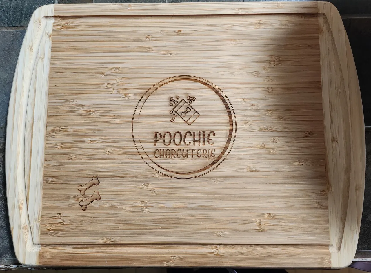 A wooden cutting board with the name poochie on it.